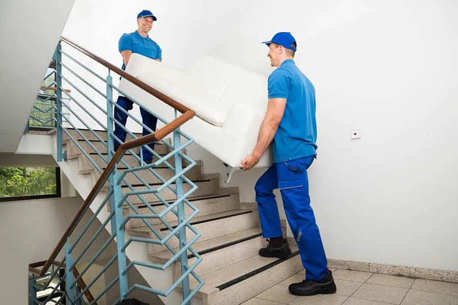 Professional movers carrying a sofa up a flight of stairs