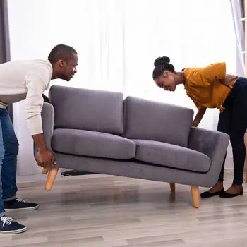 Woman holding her back while trying to lift a heavy couch with her husband