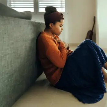 Woman sitting on a bedroom floor with a contemplative look
