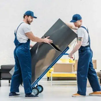 Professional movers securing a refrigerator onto a dolly in a room full of packed boxes